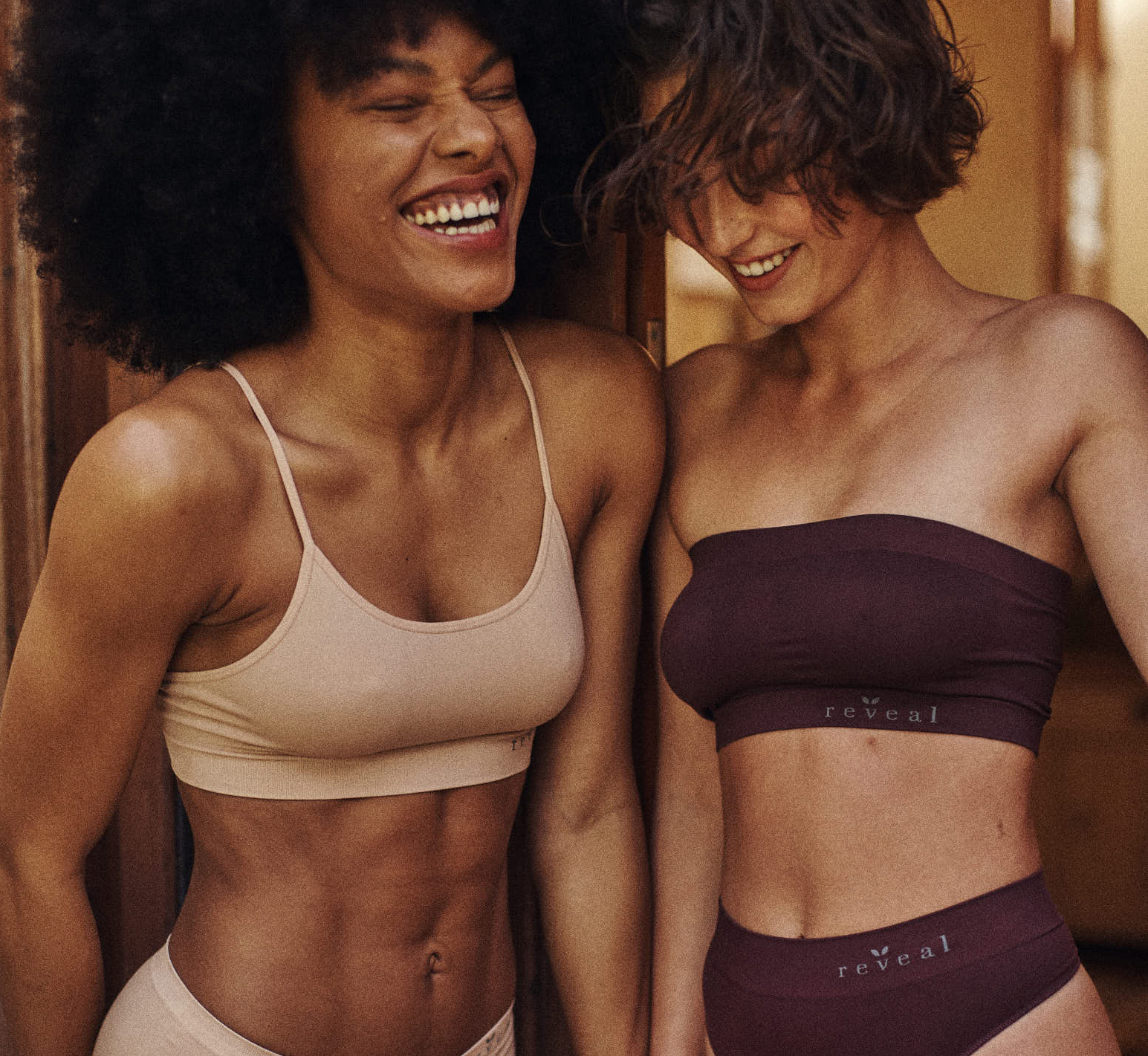 Two women laughing while wearing Reveal bra and panty sets.
