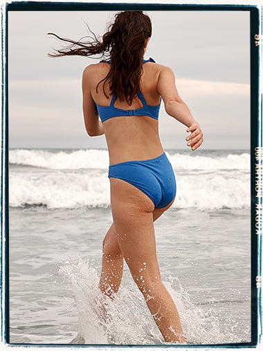 Woman running through waves in a blue bikini