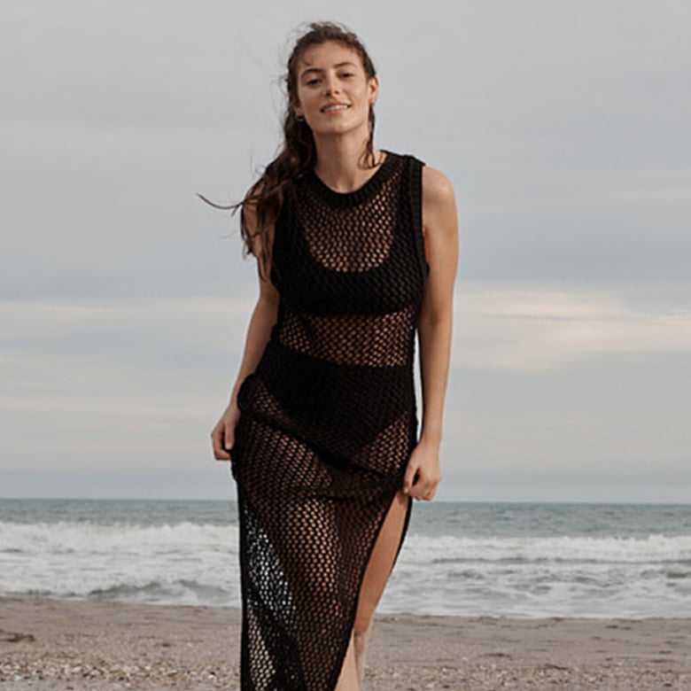 woman in black crochet cover-up dress over black a black bikini walking on a beach