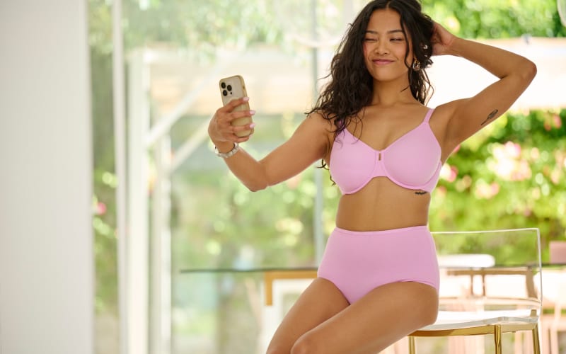 Woman in pink two-piece bikini swimwear posing for a selfie inside a modern poolside cabana.